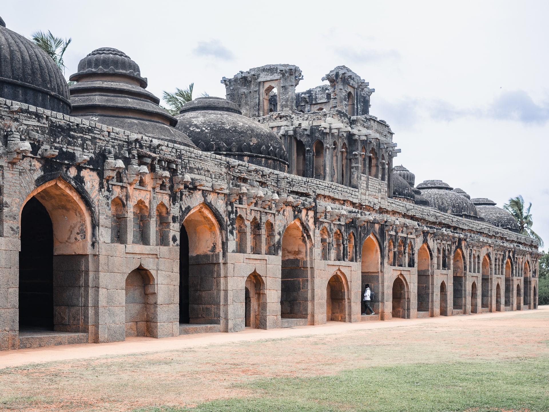 A long row of domed stone chambers with tall arched openings, a small figure walking past for scale.