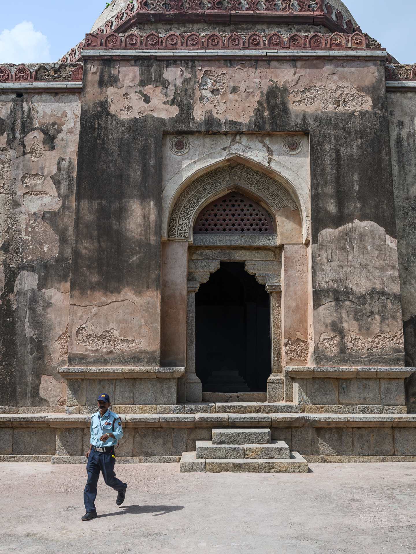 A uniformed guard walks in front of a weathered stone tomb with an ornate pointed doorway.