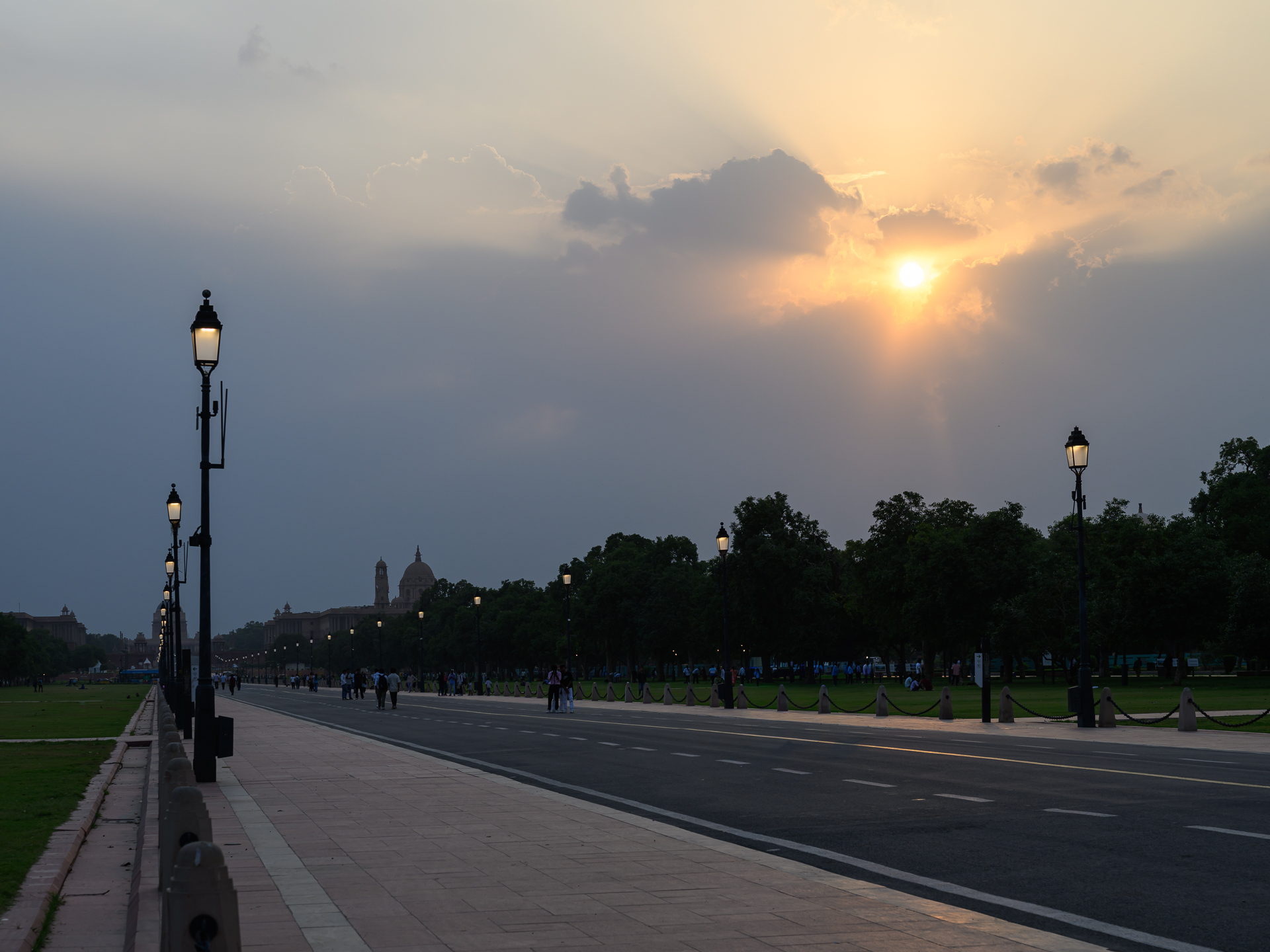 Street lamps and pedestrians line Kartavya Path beneath a break in heavy storm clouds.