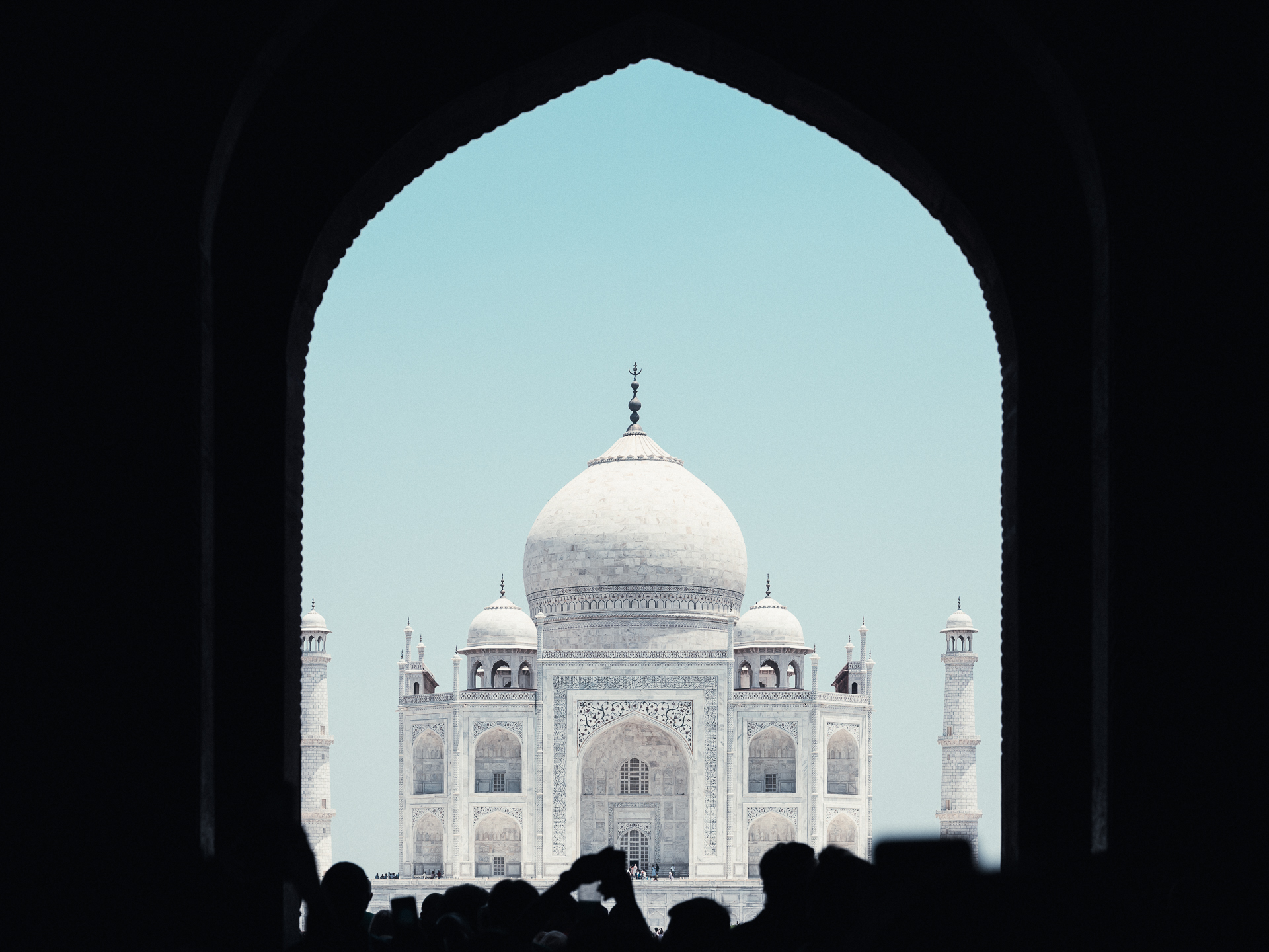 The Taj Mahal framed by a dark pointed arch, with visitors silhouetted along the lower edge.