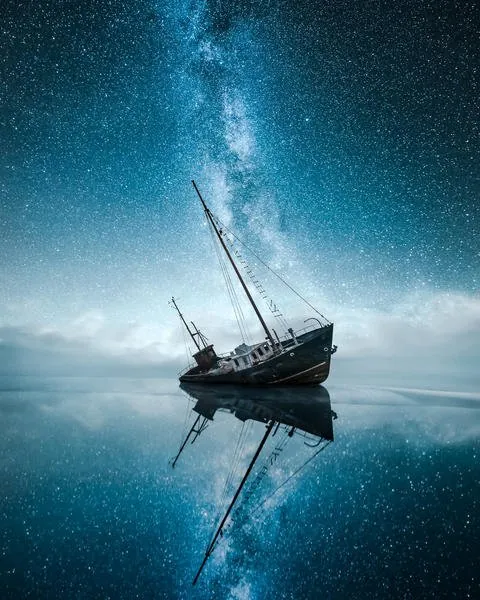 Night sky over a stranded boat reflected in calm water from the Edge gallery by Mikko Lagerstedt