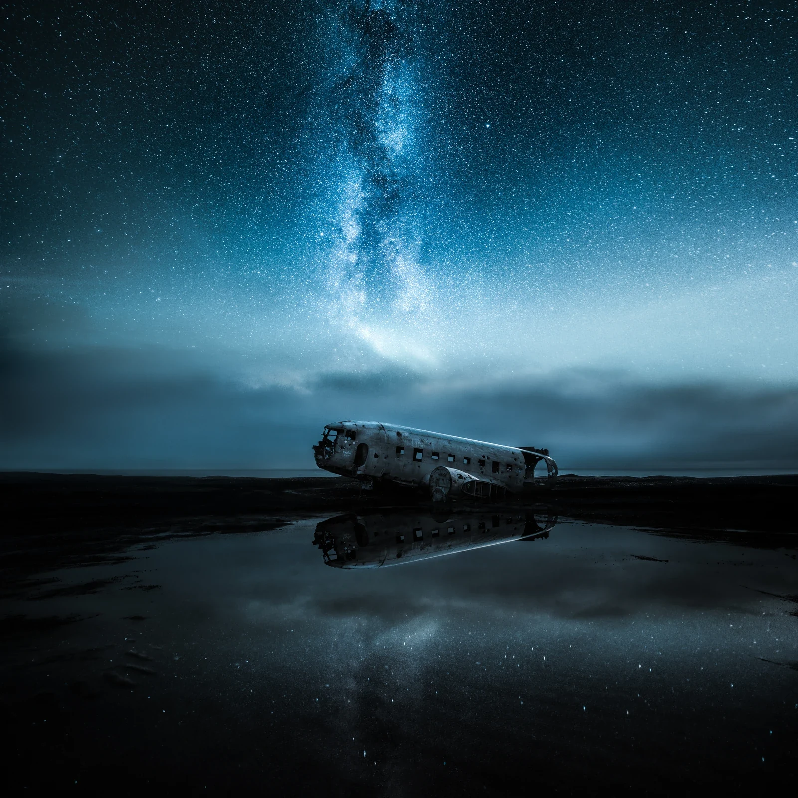 Plane wreck reflected in a rain puddle beneath a starry Icelandic sky