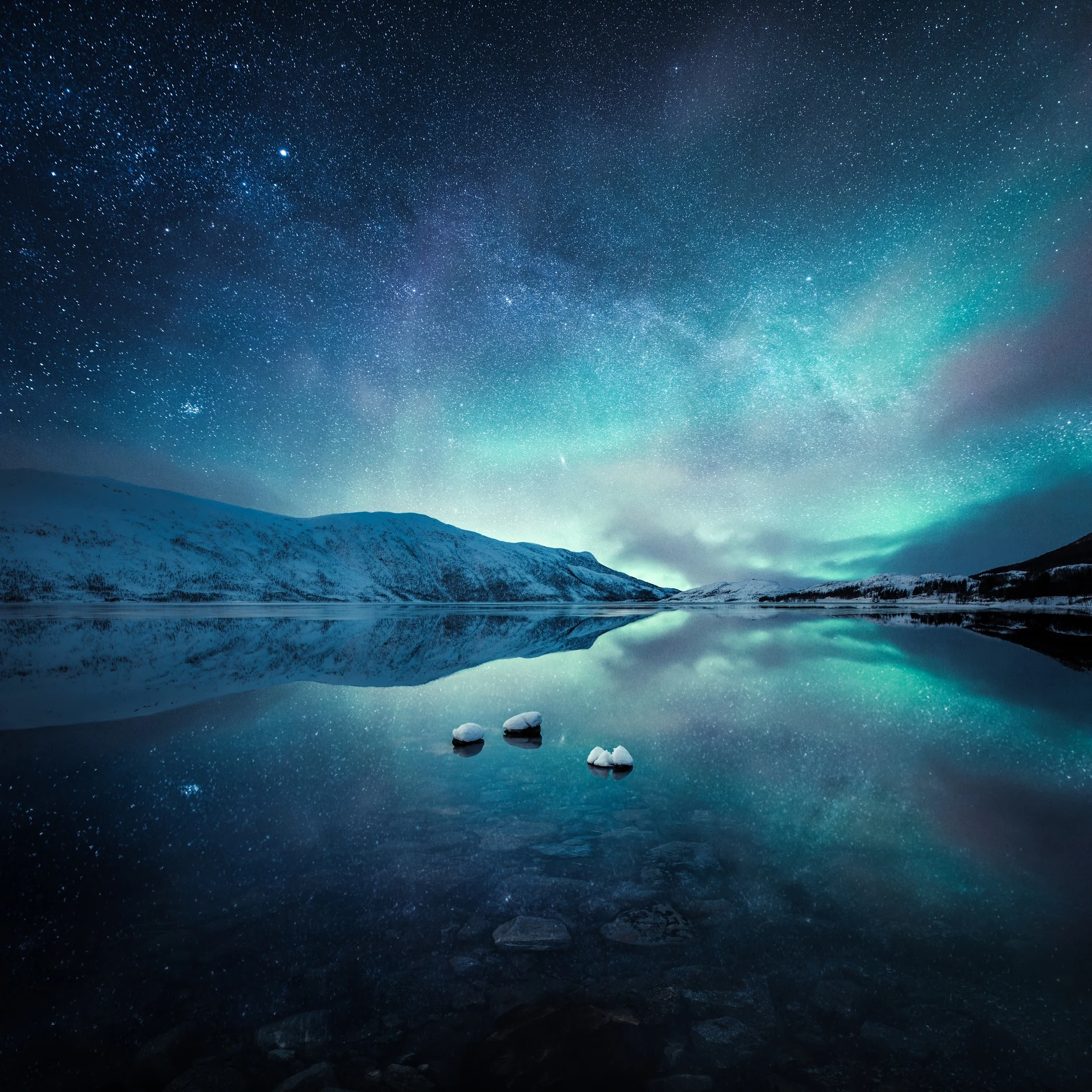 Night sky and aurora reflected in shallow still coastal water