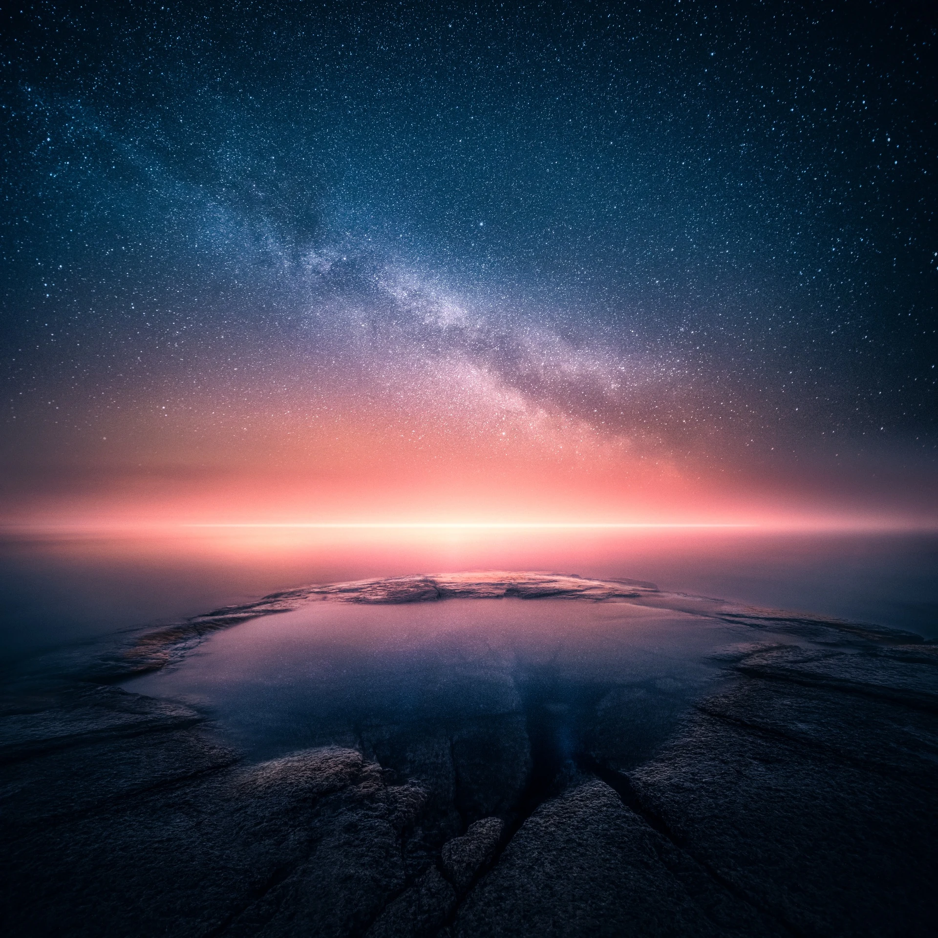 Warm sunset colours meeting a star-filled night sky over still water