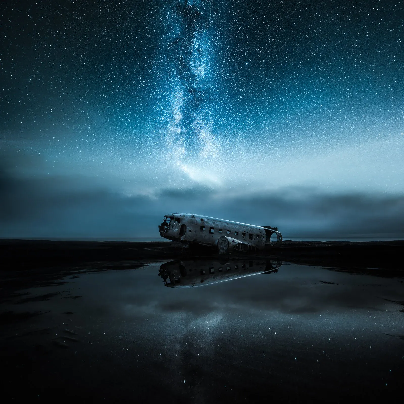 A plane wreck reflected in a rain puddle under a starry sky in Iceland